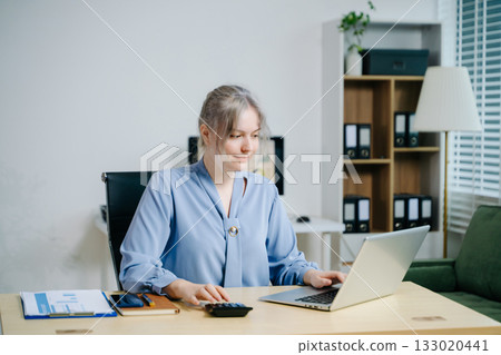 Professional businesswoman using laptop and calculator in a modern office. Perfect for finance, accounting, tax, data analysis, and corporate business concepts. 133020441