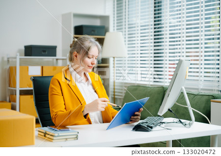 Startup small business SME, Entrepreneur owner woman using smartphone or tablet taking receive and checking online purchase shopping order to preparing pack product box. Startup small business SME, Entrepreneur owner woman using smartphone or tablet taking receive and checking online purchase shopping order to preparing pack product box. 133020472