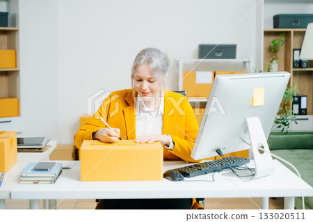 Young female entrepreneur running an SME, packing products, managing online store, shipping orders, and working from home. Perfect for ecommerce, delivery, and business themes. Young female entrepreneur running an SME, packing products, managing online store, shipping orders, and working from home. Perfect for ecommerce, delivery, and business themes. 133020511