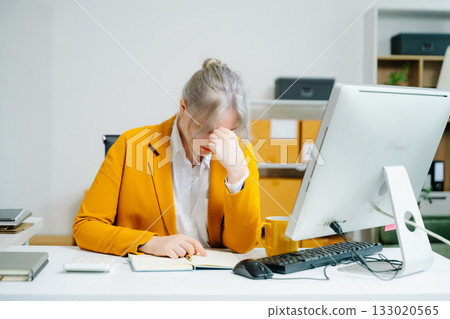 Young female SME worker in yellow blazer feeling tired and stressed while working at office desk. Facing burnout, deadline pressure, and mental fatigue. Young female SME worker in yellow blazer feeling tired and stressed while working at office desk. Facing burnout, deadline pressure, and mental fatigue. 133020565