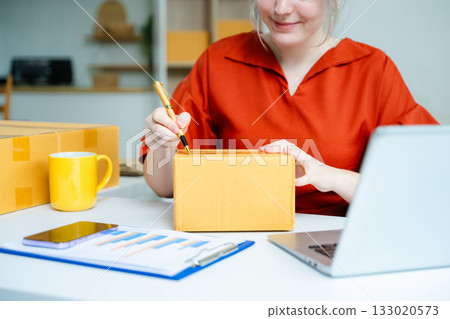 Closeup of young Caucasian woman preparing cardboard box for shipping in a home office. E-commerce, small business, and remote work concept 133020573