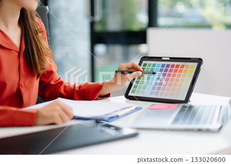 Asian graphic designer working on digital tablet with color swatches on screen. Concept of creativity, freelance design, digital content creation 133020600
