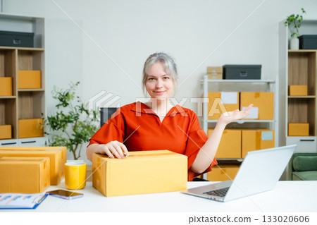 Young Caucasian woman celebrating a successful online business at home, surrounded by boxes and laptop. E-commerce, entrepreneur, and shipping concept Young Caucasian woman celebrating a successful online business at home, surrounded by boxes and laptop. E-commerce, entrepreneur, and shipping concept 133020606
