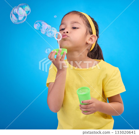 Children, blue background and a girl blowing bubbles in studio for fun or child development of motor skills. Kids, game or soap and a cute or adorable female child playing with a bubble wand Children, blue background and a girl blowing bubbles in studio for fun or child development of motor skills. Kids, game or soap and a cute or adorable female child playing with a bubble wand 133020641