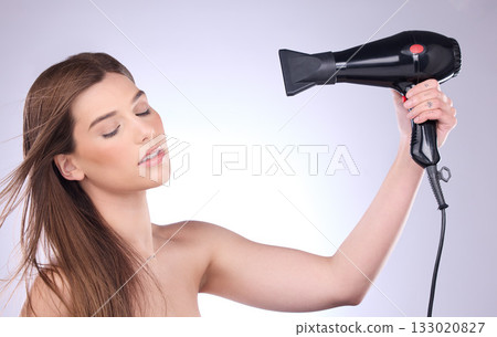 Beauty, hair dryer and a woman blowing her hairstyle in studio on a gray background for grooming or style. Salon, cosmetics and appliance with an attractive young female using heat to blowdry Beauty, hair dryer and a woman blowing her hairstyle in studio on a gray background for grooming or style. Salon, cosmetics and appliance with an attractive young female using heat to blowdry 133020827
