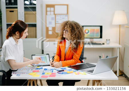 UX UI designers working with color palettes, wireframes, and digital tablets in modern office. Creative teamwork, planning, branding and design strategy 133021156