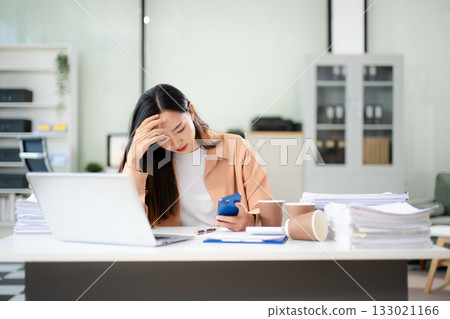 Asian businesswoman suffering headache from stress and work pressure. Holding head in pain at office desk Asian businesswoman suffering headache from stress and work pressure. Holding head in pain at office desk 133021166