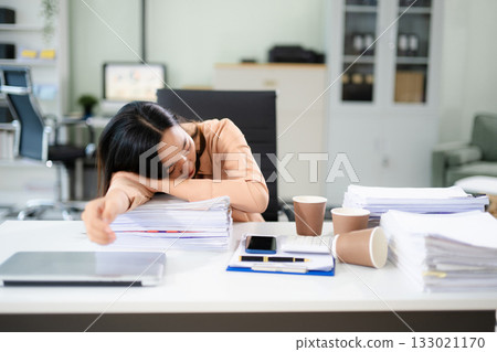 verworked Asian woman falls asleep on desk with paperwork, laptop, and coffee. Office fatigue, deadline stress, and burnout concept verworked Asian woman falls asleep on desk with paperwork, laptop, and coffee. Office fatigue, deadline stress, and burnout concept 133021170