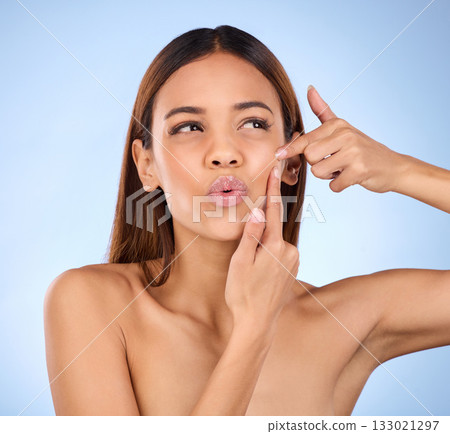 Skincare, squeeze pimple and woman with natural cosmetics, dermatology and girl against blue studio background. Female, lady and model with acne, pop blackhead and facial scar with expression on face 133021297