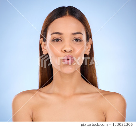 Beauty, cosmetics portrait and lips kiss with a model pout with lip gloss makeup in studio. Cosmetic, mouth and natural glow of a woman with clear and smooth skin with isolated blue background 133021306