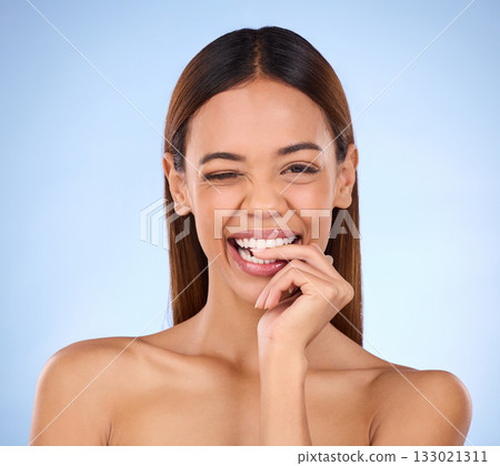 Beauty, woman and biting finger and wink portrait for skincare dermatology cosmetics in studio. Female model person on blue background for self care, facial glow and healthy or clean skin with smile Beauty, woman and biting finger and wink portrait for skincare dermatology cosmetics in studio. Female model person on blue background for self care, facial glow and healthy or clean skin with smile 133021311