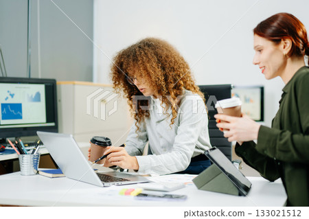 Two smiling women clinking coffee cups in a startup office, celebrating teamwork, friendship, and business success Two smiling women clinking coffee cups in a startup office, celebrating teamwork, friendship, and business success 133021512