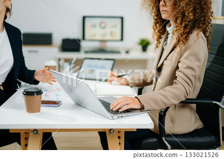 Two female professionals in smart casual outfits collaborate over finance charts and reports in a creative office space, planning business strategies 133021526