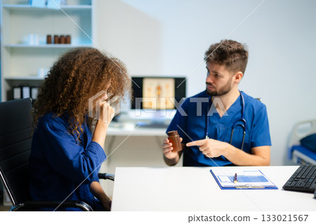 Young doctor in blue scrubs explains medicine usage to a thoughtful female patient in a clinic. 133021567