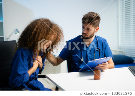 Young doctor in blue scrubs explains medicine usage to a thoughtful female patient in a clinic. Young doctor in blue scrubs explains medicine usage to a thoughtful female patient in a clinic. 133021570