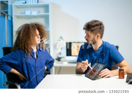 Doctor consults patient and explains knee x-ray results using tablet in clinic. Concept of medical technology, diagnosis, patient care Doctor consults patient and explains knee x-ray results using tablet in clinic. Concept of medical technology, diagnosis, patient care 133021593
