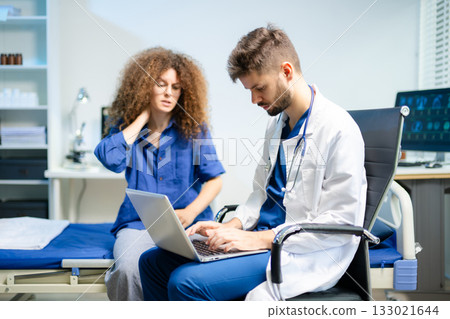 Young doctor consults female patient using a laptop in a bright clinic. Health checkup, empathy, and digital medical care Young doctor consults female patient using a laptop in a bright clinic. Health checkup, empathy, and digital medical care 133021644
