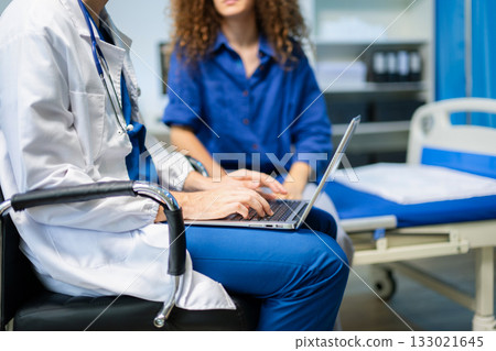Young doctor consults female patient using a laptop in a bright clinic. Health checkup, empathy, and digital medical care Young doctor consults female patient using a laptop in a bright clinic. Health checkup, empathy, and digital medical care 133021645