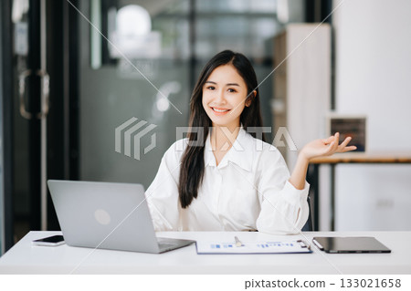 Asian businesswoman working with working notepad, tablet and laptop documents talking on the tablet and laptop Asian businesswoman working with working notepad, tablet and laptop documents talking on the tablet and laptop 133021658