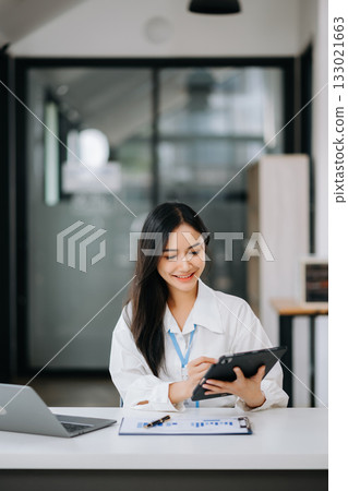 Beautiful Asian business woman typing laptop and tablet Placed at the table at office 133021663