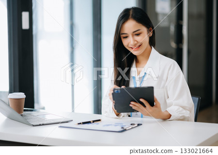 Asian businesswoman working with working notepad, tablet and laptop documents talking on the tablet and laptop 133021664