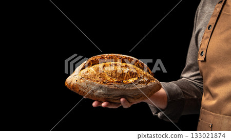 Baker holding freshly baked rustic bread loaf on black background, close up, copy space Baker holding freshly baked rustic bread loaf on black background, close up, copy space 133021874