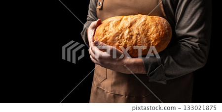 Baker holding freshly baked golden bread loaf on black background, copy space Baker holding freshly baked golden bread loaf on black background, copy space 133021875
