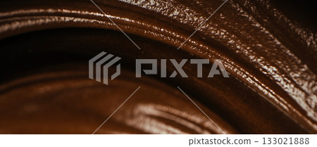 Macro close-up of melted dark chocolate with glossy texture and smooth swirls, abstract background of creamy liquid chocolate for dessert design and confectionery concept 133021888