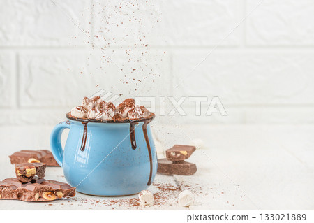 Cup of hot chocolate with marshmallows and cocoa powder splash in blue mug on white background, cozy winter drink concept with chocolate pieces and copy space for advertising design Cup of hot chocolate with marshmallows and cocoa powder splash in blue mug on white background, cozy winter drink concept with chocolate pieces and copy space for advertising design 133021889