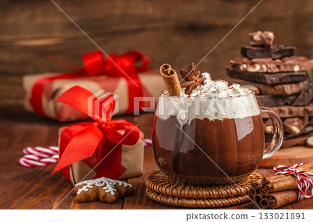 Cup of hot chocolate with whipped cream, cinnamon stick and star anise on rustic wooden table, Christmas composition with gifts and chocolate pieces, cozy festive atmosphere for winter holiday design Cup of hot chocolate with whipped cream, cinnamon stick and star anise on rustic wooden table, Christmas composition with gifts and chocolate pieces, cozy festive atmosphere for winter holiday design 133021891