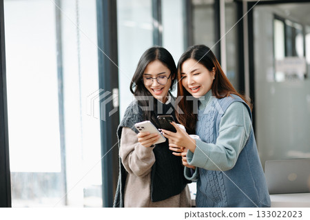 Two Attractive young Asian female college students working on the school project using laptop computer and tablet together, enjoy talking 133022023