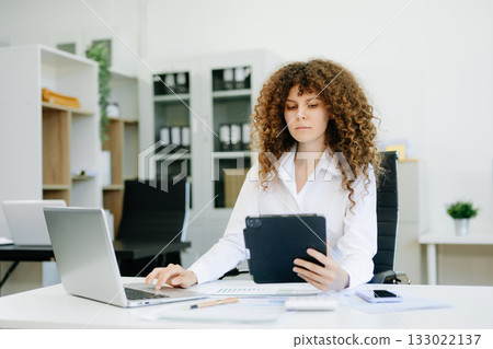 Successful businesswoman in office working on laptop.for doing math finance on an office desk, tax, report Successful businesswoman in office working on laptop.for doing math finance on an office desk, tax, report 133022137