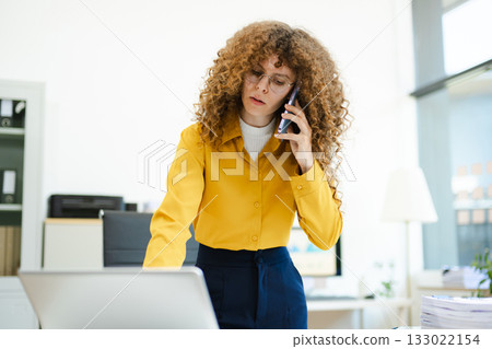 Confident businesswoman analyzing data on tablet at modern office desk with coffee, documents, and laptop. Concept of digital work 133022154
