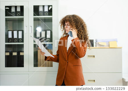 Focused businesswoman working on laptop while holding tablet at desk with documents and coffee. Concept of productivity, multitasking Focused businesswoman working on laptop while holding tablet at desk with documents and coffee. Concept of productivity, multitasking 133022229