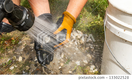 Hands of a worker using a pressure washer to clean gravel and stones, showcasing the effectiveness of outdoor cleaning techniques and tools 133022528
