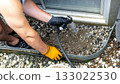 Individual using a hose to clean gravel drainage area beside a house, showcasing outdoor maintenance and water management techniques 133022530