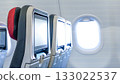 Airplane interior featuring empty passenger seats with personal screens and a bright window, creating a serene travel atmosphere with copy space 133022537
