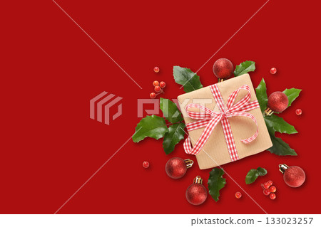 Gift sits on red background surrounded by festive decorations Gift sits on red background surrounded by festive decorations 133023257