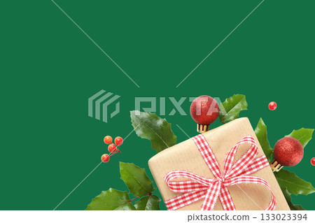 Gift with red ribbon among holly and ornaments Gift with red ribbon among holly and ornaments 133023394