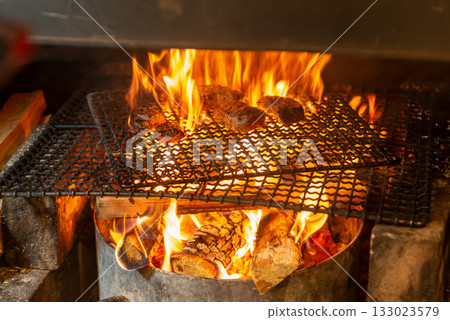 Meat dishes grilled over a wood fire - The immersive experience of a charcoal grill with rising flames 133023579