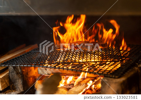 Meat dishes grilled over a wood fire - The immersive experience of a charcoal grill with rising flames Meat dishes grilled over a wood fire - The immersive experience of a charcoal grill with rising flames 133023581