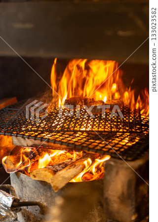 Meat dishes grilled over a wood fire - The immersive experience of a charcoal grill with rising flames 133023582