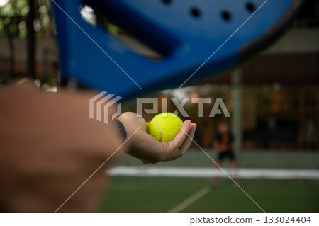 Hand holding a yellow ball ready to serve on a padel court 133024404
