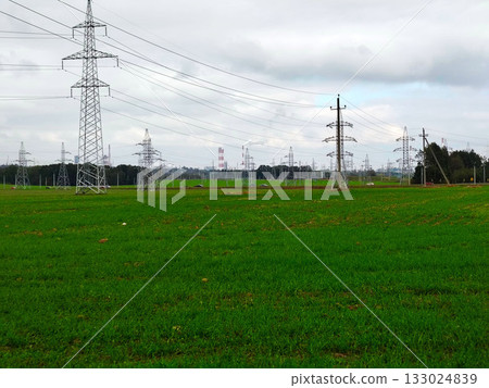 High voltage power lines and towers over green field. High voltage power lines and towers over green field. 133024839