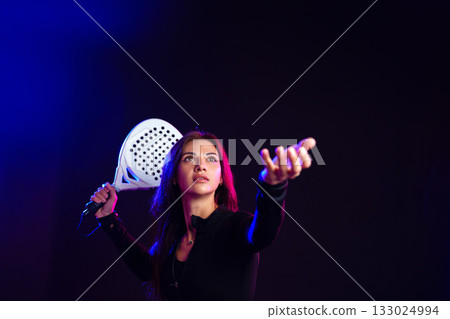Young woman practicing paddle tennis in studio with dramatic lighting and focused expression Young woman practicing paddle tennis in studio with dramatic lighting and focused expression 133024994