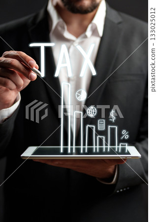 Businessman presenting tax data on a digital tablet with graphs and symbols 133025012