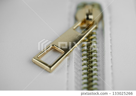 Close-up view of a gold zipper on white cloth. Close-up view of a gold zipper on white cloth. 133025266