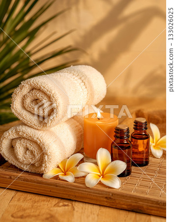 Rolled towels, aromatherapy essential oil bottles, plumeria flowers, and a lit candle on a bamboo mat for relaxation. Rolled towels, aromatherapy essential oil bottles, plumeria flowers, and a lit candle on a bamboo mat for relaxation. 133026025