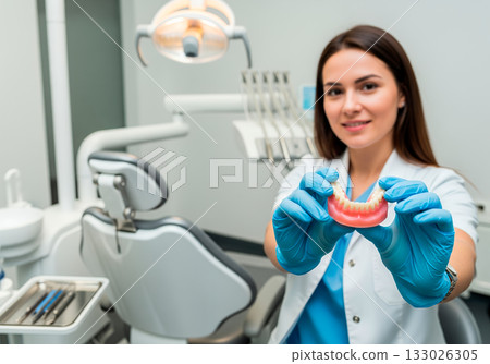 Female asian young dentist holding denture in modern clinic setting 133026305