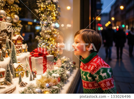 A young boy in a festive sweater gazes with joy at a Christmas display in a shop window, captivated by the holiday magic 133026496